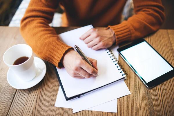 Person writing in a journal while sitting at a wooden table